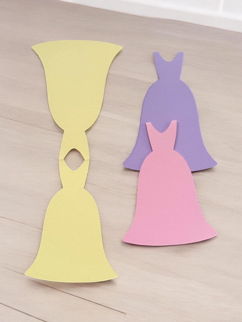 Pu&ograve; includere: Tre sagome di abiti di carta, uno giallo, uno rosa e uno viola. L'abito giallo &egrave; diviso a met&agrave;, con la parte superiore separata dalla parte inferiore.