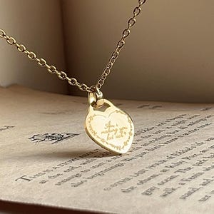 Può includere: Collana color oro con un ciondolo a forma di cuore. Il ciondolo presenta l'iscrizione "Am I making you feel sick?" in un carattere delicato, circondato da un motivo floreale. La collana è esposta su una pagina di libro vintage.