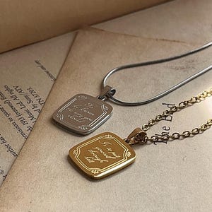 Può includere: Due collane con pendente rettangolare, una in metallo color argento con catena a serpente e una in metallo color oro con catena a maglie. Ogni pendente presenta un bordo decorato e un testo inciso in corsivo: "Is to put yourself through hell."