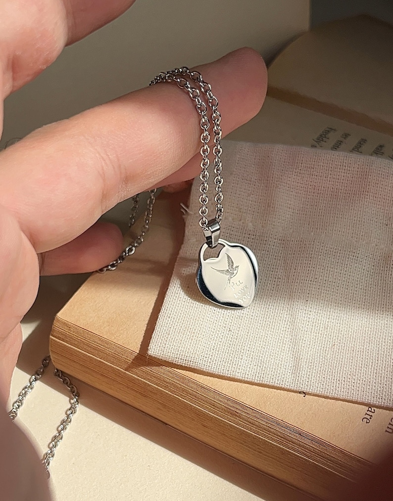 Pu&ograve; includere: Una collana d'argento con un ciondolo a forma di cuore. Il ciondolo presenta un piccolo disegno di un uccello e le parole "Ti amo" incise su di esso.