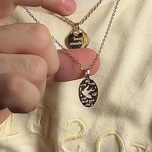 Peut inclure: Deux colliers en or avec des pendentifs. Le collier du haut a un pendentif en forme de c&oelig;ur avec le texte "baby wannabe" inscrit dessus. Le collier du bas a un pendentif rond avec un motif d'oiseau et du texte en arabe.
