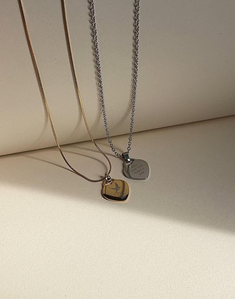 Pu&ograve; includere: Due delicate collane con ciondoli a forma di cuore. La collana dorata presenta un piccolo design di uccello sul ciondolo. La collana d'argento ha un ciondolo con l'iscrizione "Till the day that I die."