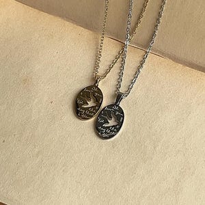 Peut inclure: Deux colliers en argent avec des pendentifs ovales. Les pendentifs pr&eacute;sentent une d&eacute;coupe de deux oiseaux en vol et le texte "till the day that I die I love you".