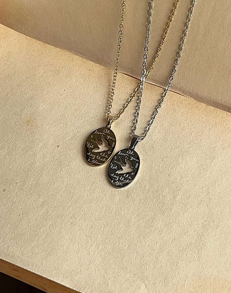 Peut inclure: Deux colliers en argent avec des pendentifs ovales. Les pendentifs pr&eacute;sentent une d&eacute;coupe de deux oiseaux en vol et le texte "till the day that I die I love you".