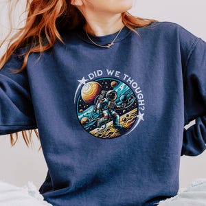 May include: A navy blue sweatshirt with a graphic of an astronaut in space. The graphic includes planets, stars, and the text "Did we though?"