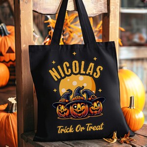 Könnte beinhalten: Schwarze Tragetasche mit einem Halloween-Motiv. Sie zeigt drei Kürbisse mit Hexenhüten vor einem Vollmond. Der Text "NICOLAS Trick or Treat" ist auf die Tasche gedruckt.