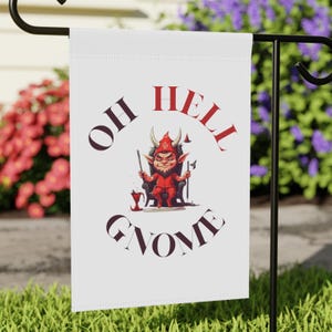 May include: A white garden flag featuring a red devil gnome seated on a throne. The flag reads "Oh Hell Gnome".