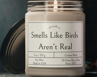 May include: A glass candle jar with a beige label that reads "sds candle co Smells Like Birds Aren't Real 9 oz/255 g Cotton Wick Soy Wax Made In USA 50 Hour Burn Time Since 2025".