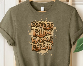 Op de afbeelding: Een groen T-shirt met een bruine grafische print die "Coffee Run Wine Repeat" zegt in een graffiti-stijl.