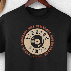 Puede incluir: Camiseta negra con un diseño de disco de vinilo vintage. El diseño incluye un tocadiscos y el texto "Vintage Records: The Timeless Soundtrack".