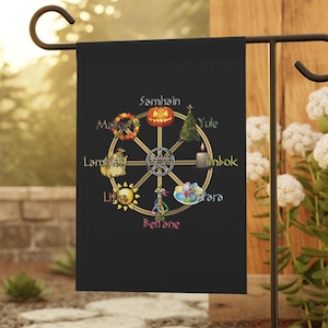 May include: A black garden flag featuring a gold wheel of the year design. The wheel has eight spokes with symbols representing the eight sabbats: Samhain, Yule, Imbolc, Ostara, Beltane, Litha, Lammas, and Mabon.