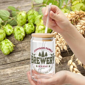 Puede incluir: Un tarro de vidrio transparente con tapa de bambú y una pajita. El tarro tiene una etiqueta que dice "Johnson Family Brewery" con un diseño de árbol de Navidad y el texto "Holiday Brews, Craft Christmas Cheers".