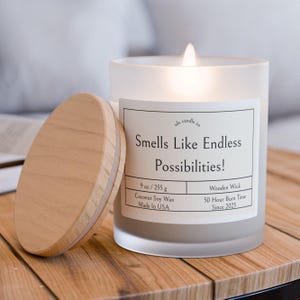 May include: A frosted glass candle jar with a wooden lid. The candle is lit and the label reads "ds candle co Smells Like Endless Possibilities! 9 oz / 255 g Coconut Soy Wax Made In USA Wooden Wick 50 Hour Burn Time Since 2025"