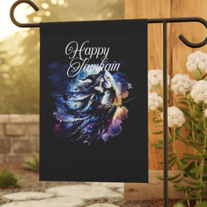 Puede incluir: Una bandera de jardín negra con una bruja volando en una escoba frente a una luna llena. El texto "Happy Samhain" está escrito en letras blancas cursivas.