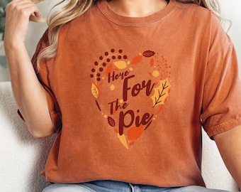 May include: A burnt orange t-shirt with a heart-shaped design featuring fall leaves and the text "Here For The Pie".