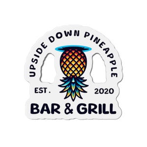以下が含まれることがあります： 黒と黄色のパイナップルが描かれた白いステッカー。パイナップルの根元は青と緑色。パイナップルは逆さまになっていて、その上に青い輪が描かれている。パイナップルの上には黒いアーチ状に「Upside Down Pineapple Bar & Grill」という文字が書かれている。パイナップルの下には「Est. 2020」という文字が書かれている。
