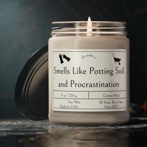 May include: A glass jar candle with a white label that reads "Smells Like Potting Soil and Procrastination". The candle is soy wax and has a cotton wick. It is 9 ounces or 255 grams and has a 50 hour burn time. The candle is made in the USA.