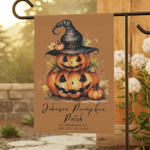 Puede incluir: Una bandera de jardín marrón con una ilustración de acuarela de tres calabazas talladas en forma de calavera apiladas. La calabaza de arriba lleva un sombrero de bruja negro. La bandera dice "Johnson Pumpkin Patch" y "123 Anywhere St., Any City, ST 12345".