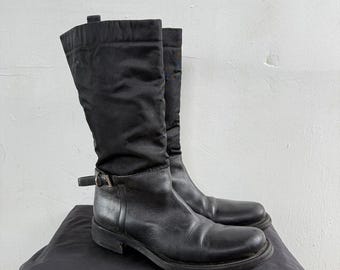 May include: Black leather and nylon knee-high boots with a buckle detail on the side.