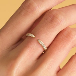 May include: A gold ring with a curved design, set with small diamonds. The ring is open on one side, allowing it to be easily slipped on and off.