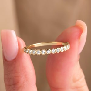 May include: A gold band ring with a row of small, round, clear gemstones.
