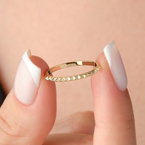 May include: A thin gold band ring with a textured design of small triangles around the entire band.
