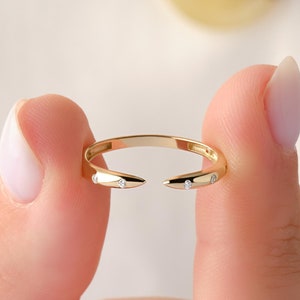 May include: A gold ring with two small diamond accents on the pointed ends. The ring is open and has a simple design.