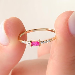 May include: A gold ring with a pink rectangular gemstone and small clear gemstones on the band.
