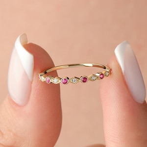 May include: A delicate gold band ring with alternating small round pink and white gemstones.