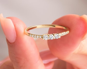May include: A delicate gold band ring with three small round diamonds and a row of smaller diamonds around the band.