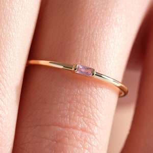 May include: A delicate gold ring with a single, small, rectangular pink gemstone set in the centre.