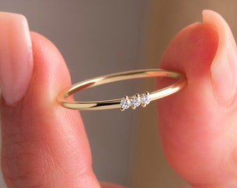 Könnte beinhalten: Ein zarter Goldring mit drei kleinen Diamanten in einer Reihe.