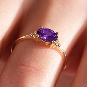 May include: A gold ring with a purple oval gemstone and small gold beads on the band.