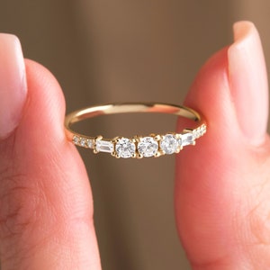 May include: A delicate gold band ring with a row of five sparkling diamonds. The center diamonds are round, while the diamonds on either side are baguette-shaped.