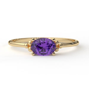 May include: A gold ring with a purple oval gemstone set in a delicate, beaded design.