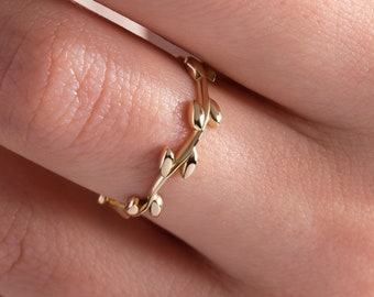 Könnte beinhalten: Ein goldener Ring mit einem zarten Design aus Blättern und Zweigen. Der Ring wird an einem Finger getragen.