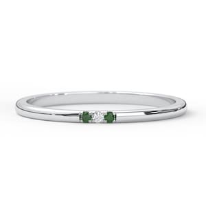 May include: A thin silver band ring with a small diamond and two green gemstones.