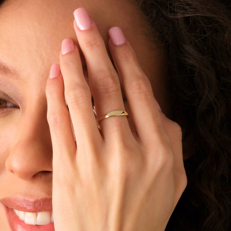 May include: A simple gold band ring with a slightly rounded shape.