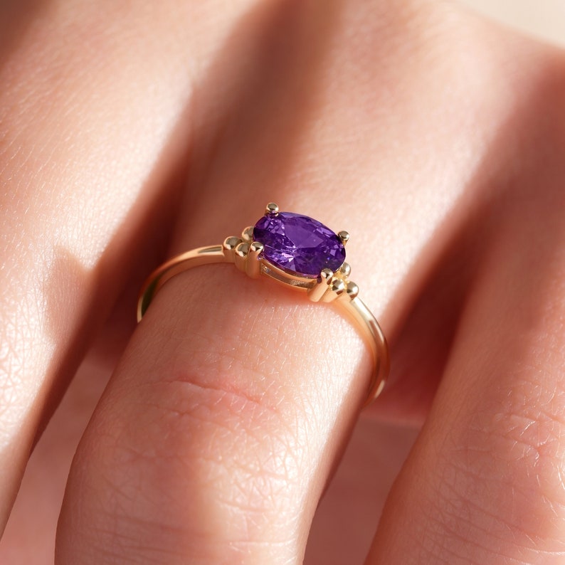 May include: A gold ring with a purple oval gemstone and small gold beads on the band.