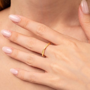 May include: A gold-toned ring with a twisted design. The ring is worn on a person's finger.