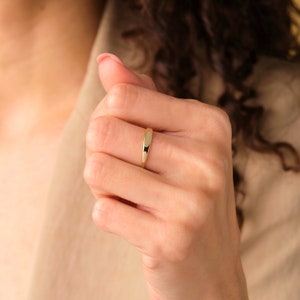 May include: A simple gold band ring with a slightly rounded top. The ring is worn on the middle finger of a person's hand.