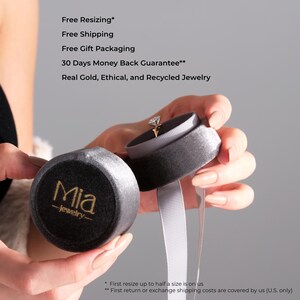 May include: A gold engagement ring with a diamond is displayed in an open gray velvet ring box. The box is held next to a closed matching box with the gold text "Mia -jewelry-". The image also includes the text "Free Resizing", "Free Shipping", "Free Gift Packaging", "30 Days Money Back Guarantee**", and "Real Gold, Ethical, and Recycled Jewelry".