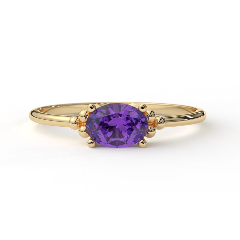 May include: A gold ring with a purple oval gemstone set in a delicate, beaded design.