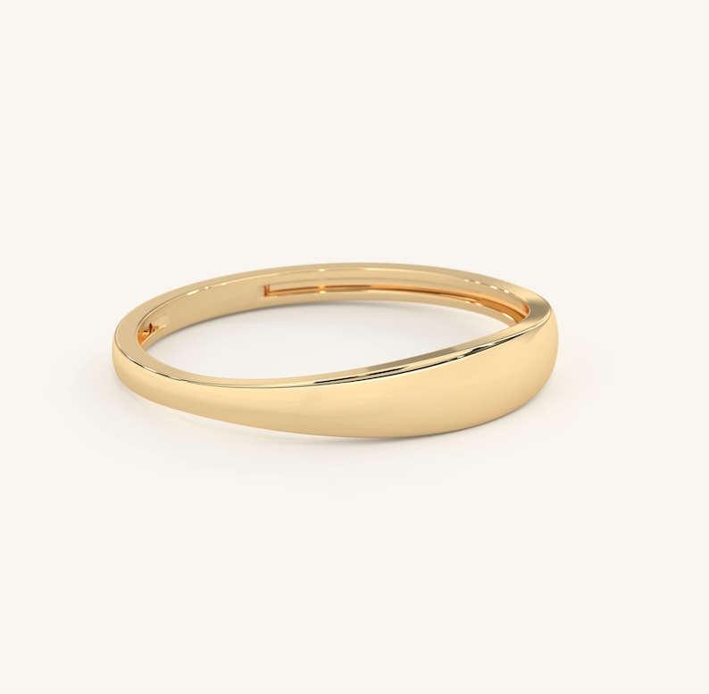 May include: A simple gold band ring with a rounded, slightly curved top. The ring is smooth and polished.