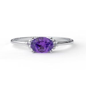 May include: A silver ring with a purple oval gemstone set in a delicate prong setting. The ring has small accents on either side of the gemstone.