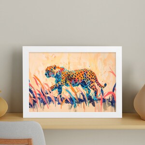 May include: A framed art print featuring a colorful watercolor painting of a cheetah walking through tall grass. The cheetah has orange and black spots with blue and yellow accents. The artwork is in a white frame.