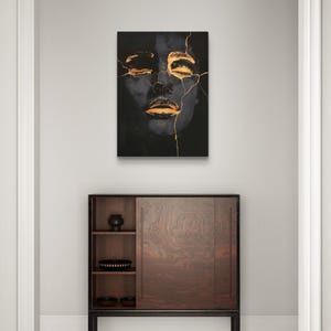 May include: A rectangular wall art print featuring a dark, monochromatic portrait of a face with closed eyes and lips, accented by bright gold-coloured cracks running across the forehead, eyes, and mouth, creating a high-contrast visual effect.