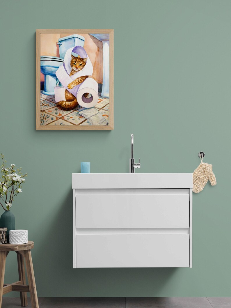 Peut inclure: Une peinture &agrave; l'aquarelle encadr&eacute;e repr&eacute;sente un chat roux en train de jouer avec des rouleaux de papier toilette dans une salle de bain. L'&oelig;uvre comprend des toilettes bleues, des carreaux de sol &agrave; motifs et un cadre en bois brun clair.