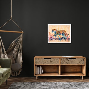 May include: A framed watercolor painting of a leopard in motion. The artwork features a colorful leopard with orange, blue, and yellow spots, set against a backdrop of tall grass. The painting is displayed on a dark wall.