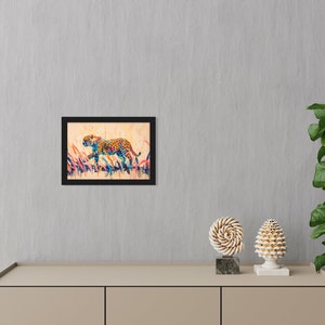 May include: Framed art print featuring a colorful cheetah illustration. The cheetah is depicted in a running pose with a spotted coat, set against a backdrop of tall grass. The artwork is framed in a black border.